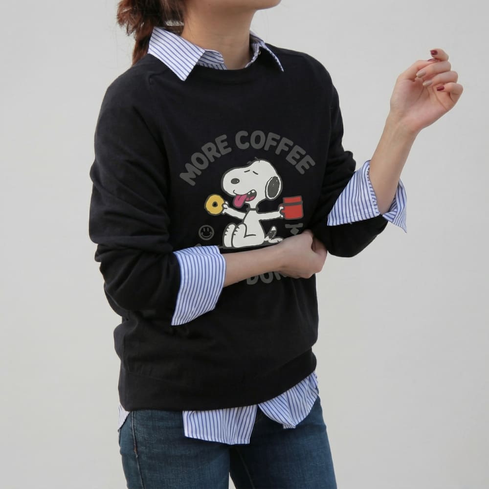 Person wearing a black sweater with a cartoon character and 'More Coffee' text, over a striped shirt.