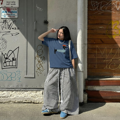 Woman wearing a blue t-shirt with a graphic design and striped pants standing against a graffiti-covered wall.