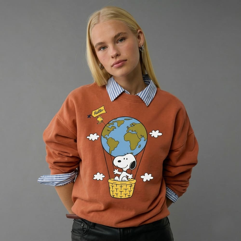 Person wearing a orange sweater with a cartoon design of Snoopy in a hot air balloon over the world.