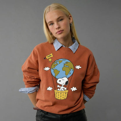 Person wearing a orange sweater with a cartoon design of Snoopy in a hot air balloon over the world.