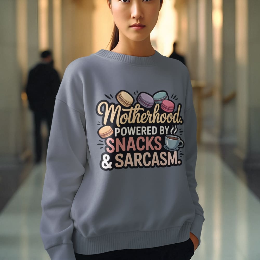 Sweatshirt design with text “Motherhood. Powered by Snacks & Sarcasm.” featuring colorful macarons and a steaming coffee cup on vintage-washed cotton fleece.