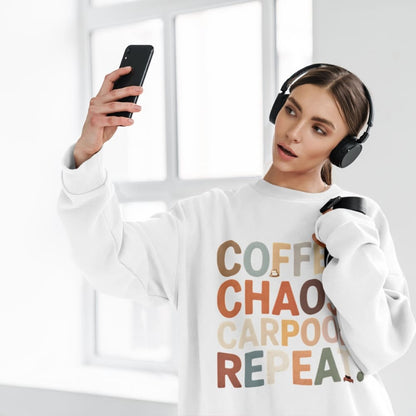 Woman wearing a white sweatshirt with colorful text, holding a phone and wearing headphones.
