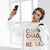 Woman wearing a white sweatshirt with colorful text, holding a phone and wearing headphones.
