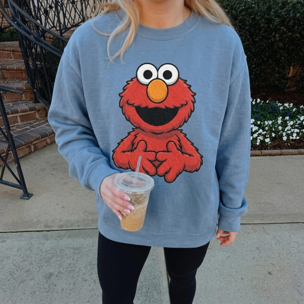 Person wearing a blue sweatshirt with a red character design, holding an iced drink.