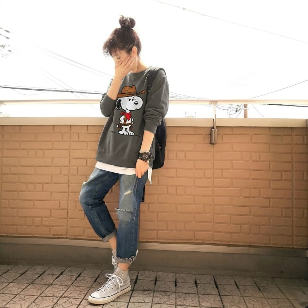 Person wearing a graphic gray sweatshirt and jeans standing against a brick wall.