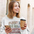 Woman wearing a sweatshirt with humorous text, holding a coffee cup and phone.