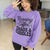 Person wearing a purple sweatshirt with text in a kitchen