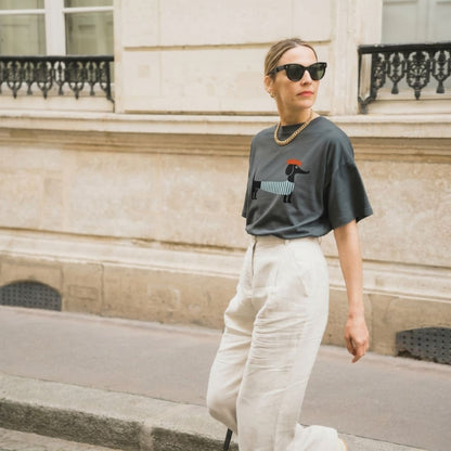 Woman wearing a dark gray t-shirt with a graphic design and light-colored pants in an urban setting.