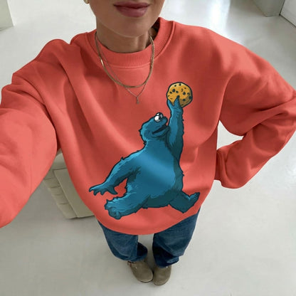 Person wearing a red sweatshirt with a blue creature holding a cookie design.