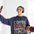 Person wearing a navy sweatshirt with colorful text, holding a phone and yoga mat indoors.