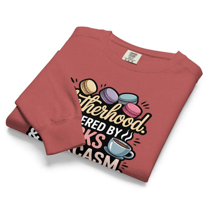 Sweatshirt design with text “Motherhood. Powered by Snacks & Sarcasm.” featuring colorful macarons and a steaming coffee cup on vintage-washed cotton fleece.