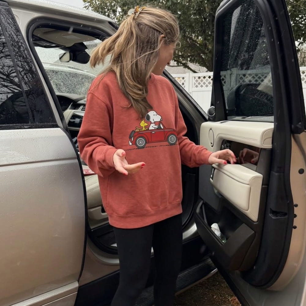 Person wearing a red sweatshirt with a graphic design, standing next to an open car door.