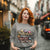 Sweatshirt design with text “Motherhood. Powered by Snacks & Sarcasm.” featuring colorful macarons and a steaming coffee cup on vintage-washed cotton fleece.