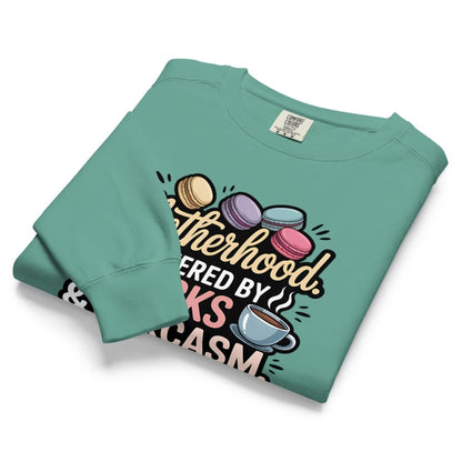 Sweatshirt design with text “Motherhood. Powered by Snacks & Sarcasm.” featuring colorful macarons and a steaming coffee cup on vintage-washed cotton fleece.