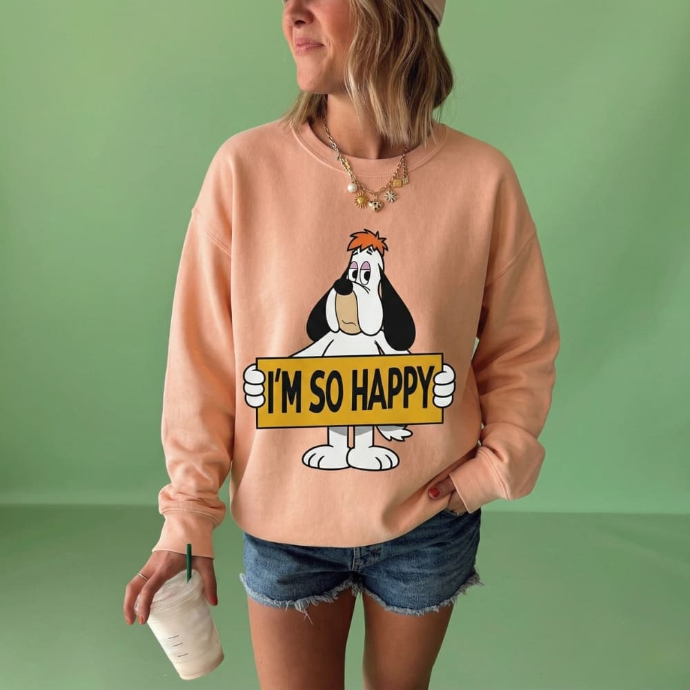 Person wearing a peach-colored sweatshirt with a cartoon character holding a 'I'm So Happy' sign on a green background