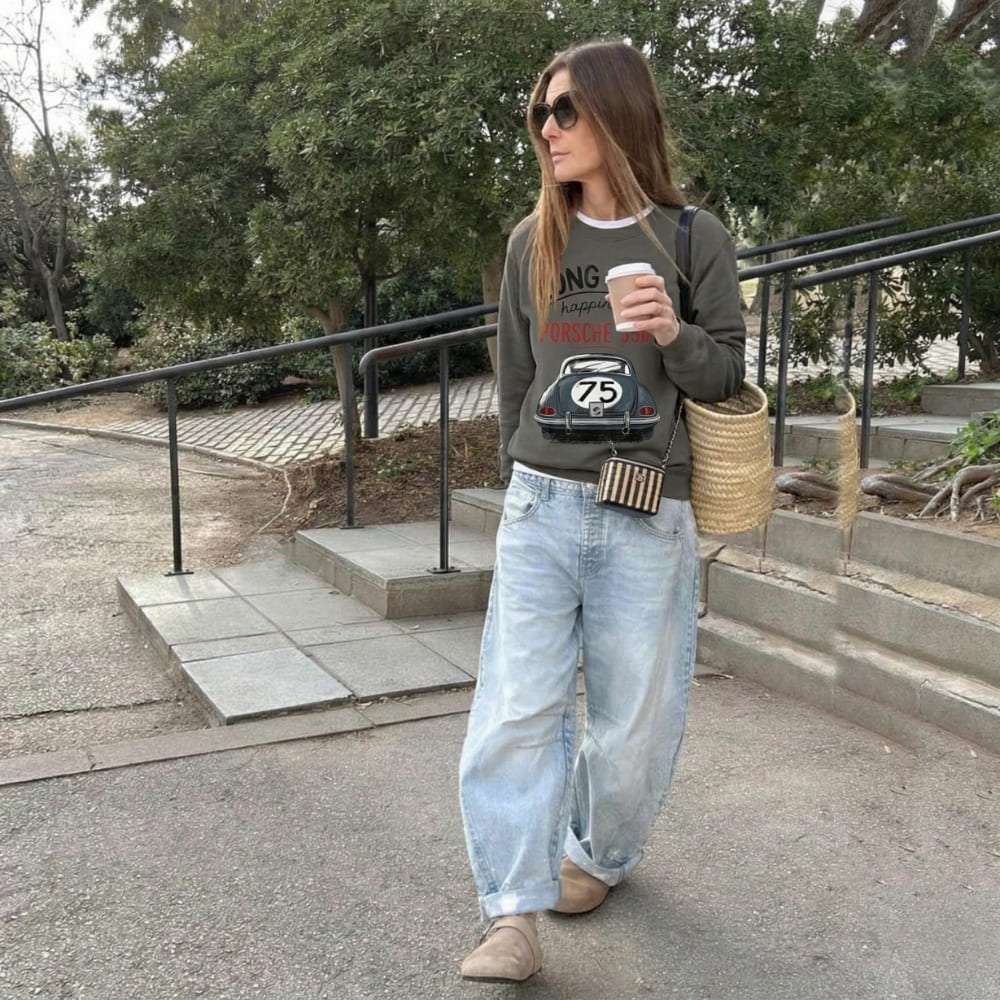 Woman walking outdoors holding a coffee cup, wearing a graphic t-shirt and jeans.