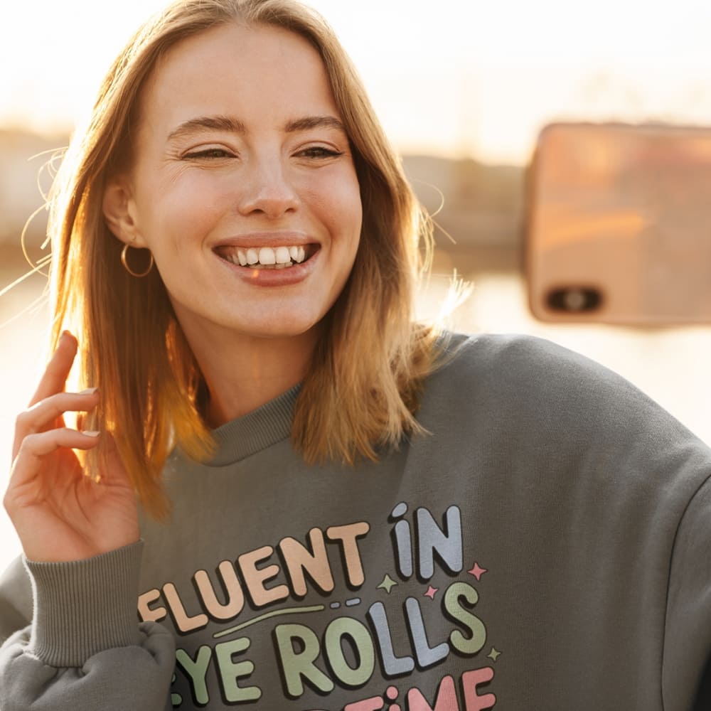 Woman wearing a sweatshirt with colorful text, smiling outdoors.
