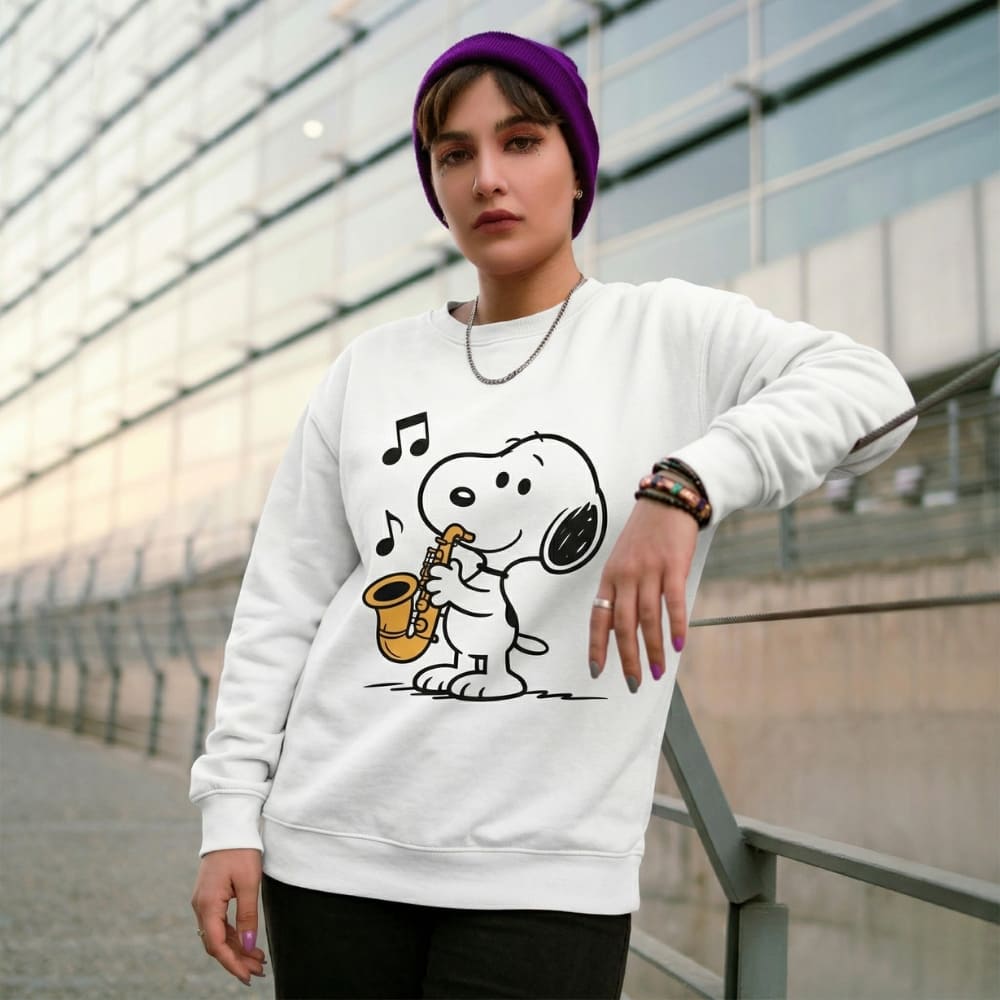 Person wearing a white sweatshirt with a cartoon character playing a saxophone, standing in front of a modern building.