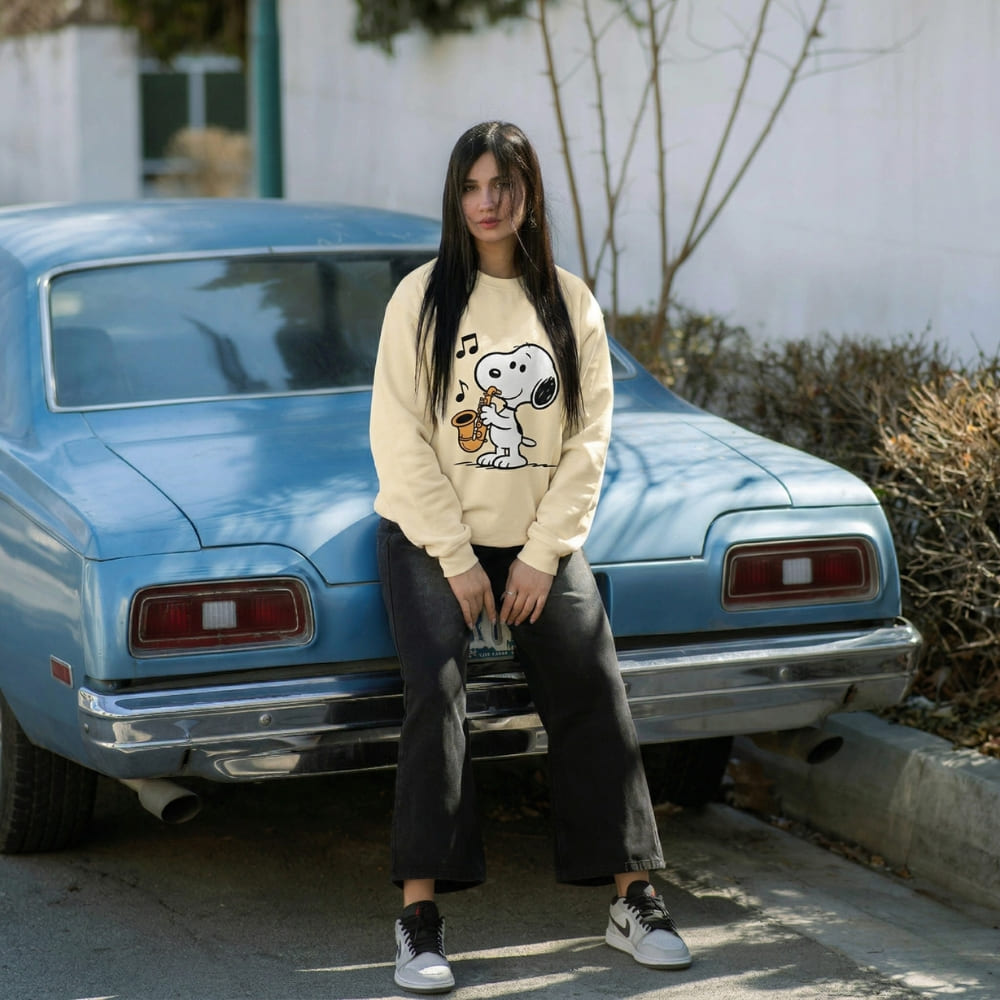 Woman wearing a beige sweatshirt with a dog graphic sitting in front of a blue vintage car.