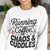 Person wearing a white sweatshirt with text 'Running on Coffee, Chaos & Cuddles' in a casual setting.