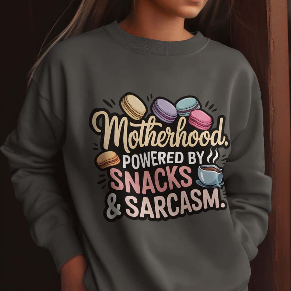Sweatshirt design with text “Motherhood. Powered by Snacks & Sarcasm.” featuring colorful macarons and a steaming coffee cup on vintage-washed cotton fleece.