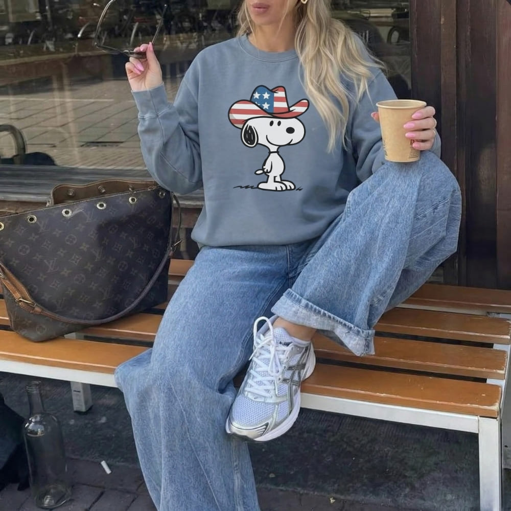 Person wearing a blue sweatshirt with a cartoon character, sitting on a bench holding a cup.
