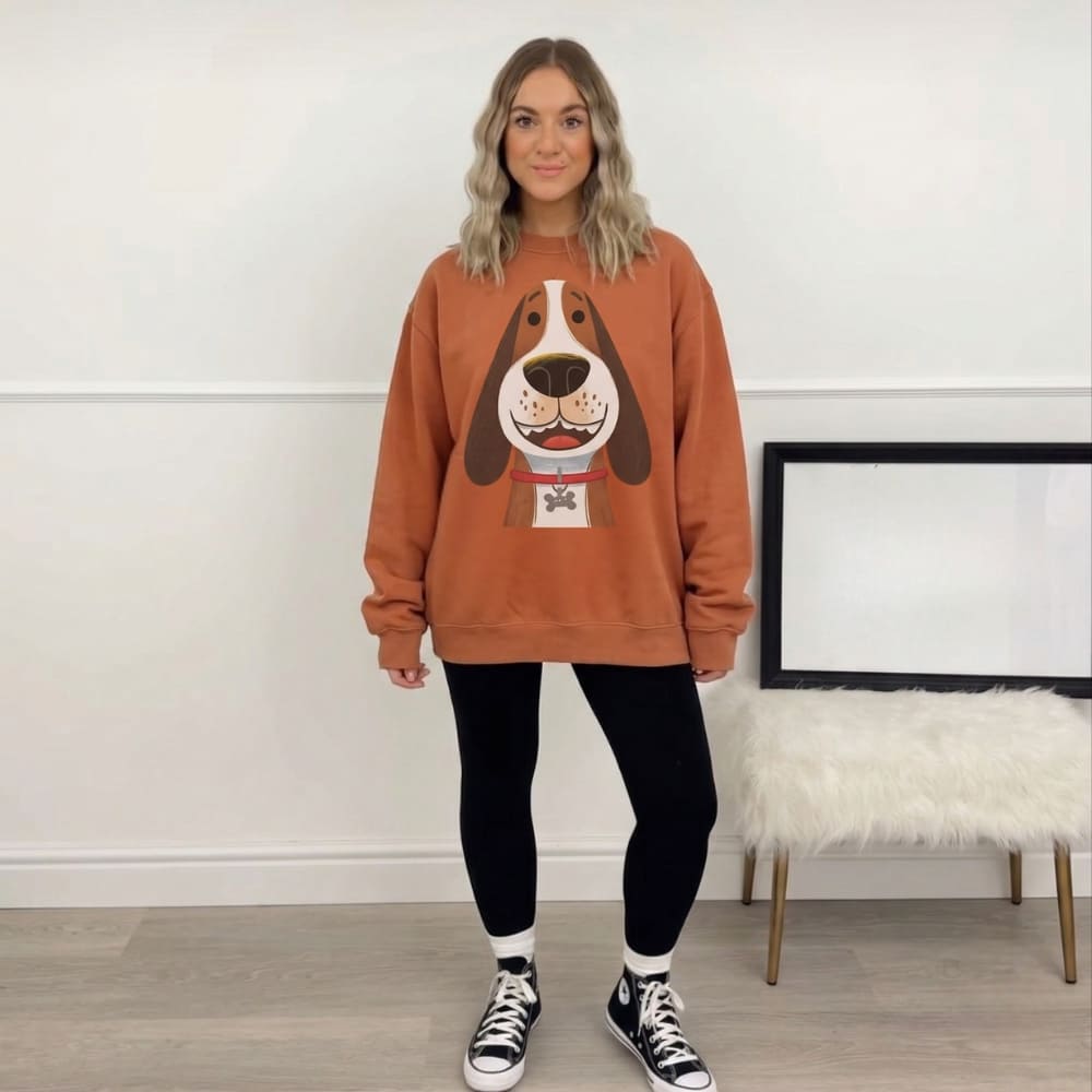 Person wearing a orange sweatshirt with a dog graphic in a room with a white wall and wooden floor.