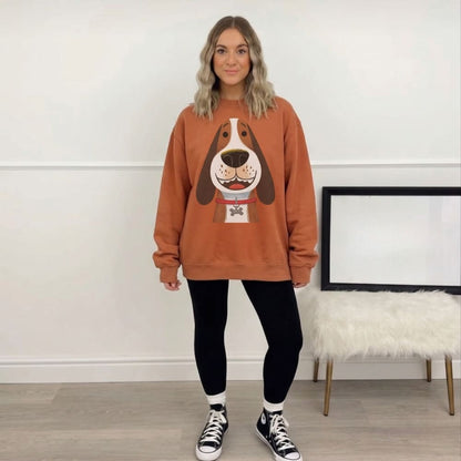 Person wearing a orange sweatshirt with a dog graphic in a room with a white wall and wooden floor.