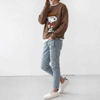 Person wearing a brown sweatshirt with a cartoon character, light blue jeans, and white sneakers on a white background