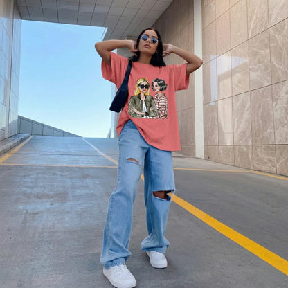 Person wearing a pink t-shirt with graphic design and blue jeans standing in an outdoor setting.