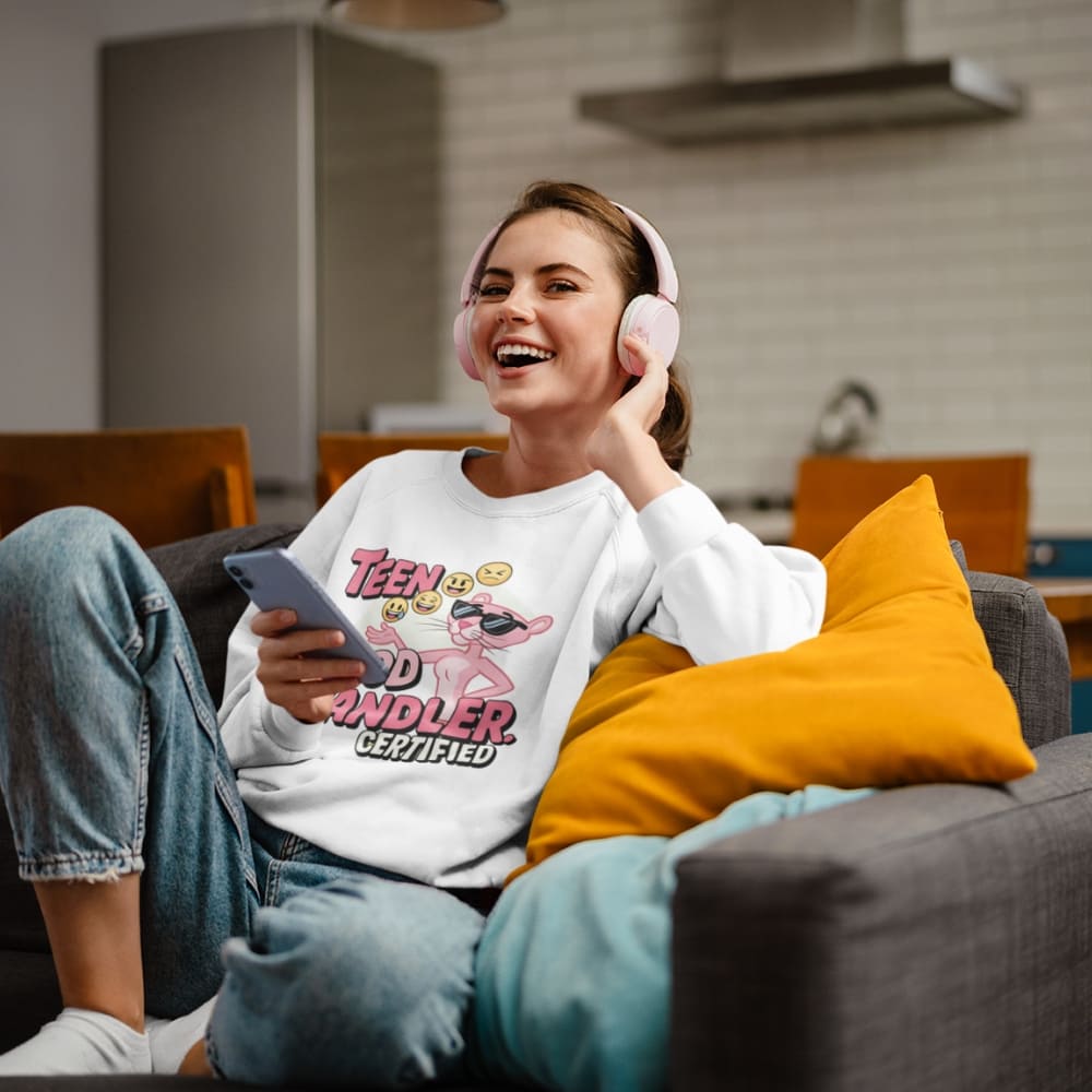 Woman sitting on a couch wearing headphones and holding a phone, with a kitchen in the background.