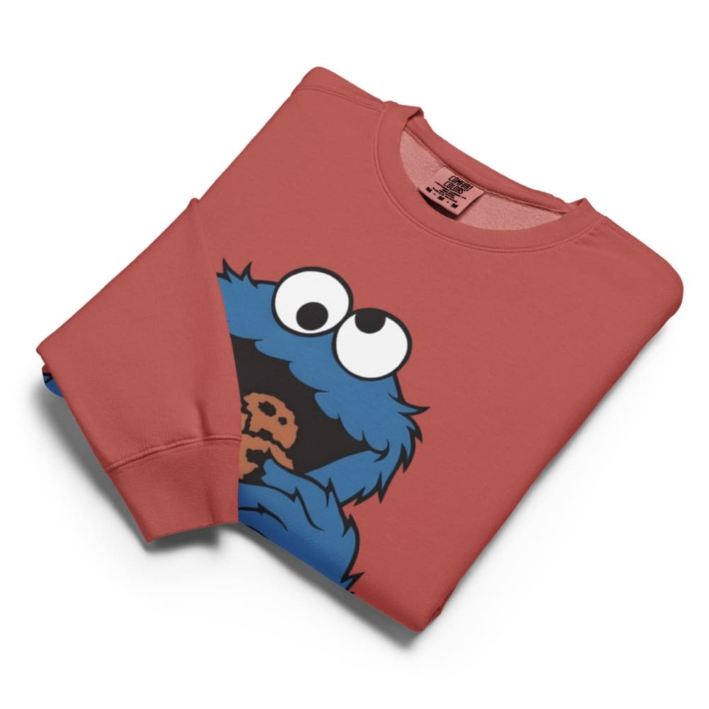 Folded red sweatshirt with a blue character holding a cookie on a white background