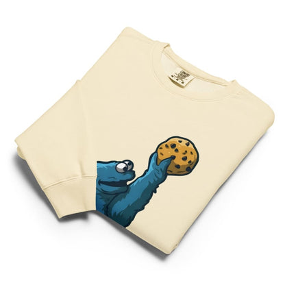 Beige sweatshirt with a blue creature holding a cookie design on a white background