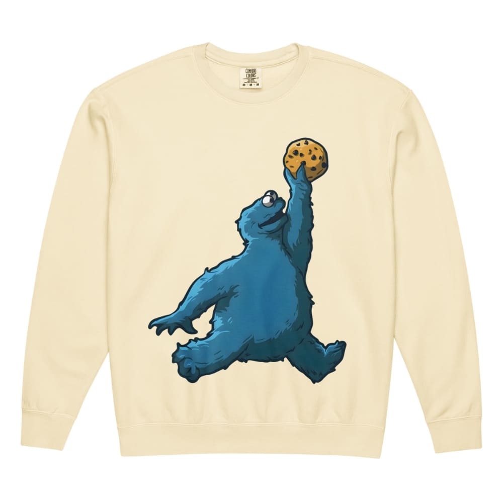 Beige sweatshirt with a blue creature holding a cookie graphic on a white background
