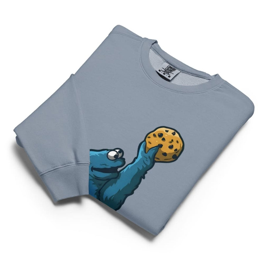 Folded blue sweatshirt with a graphic of a blue creature holding a cookie on a white background