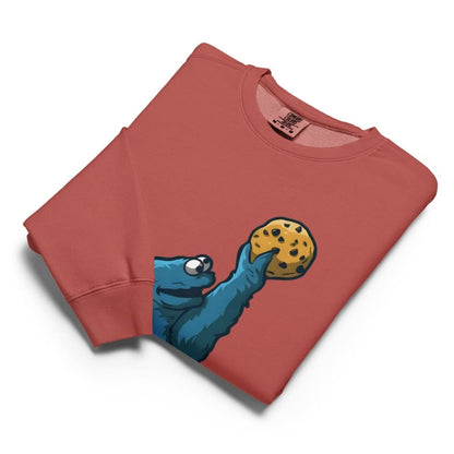 Folded red sweatshirt with a blue creature holding a cookie graphic on a white background