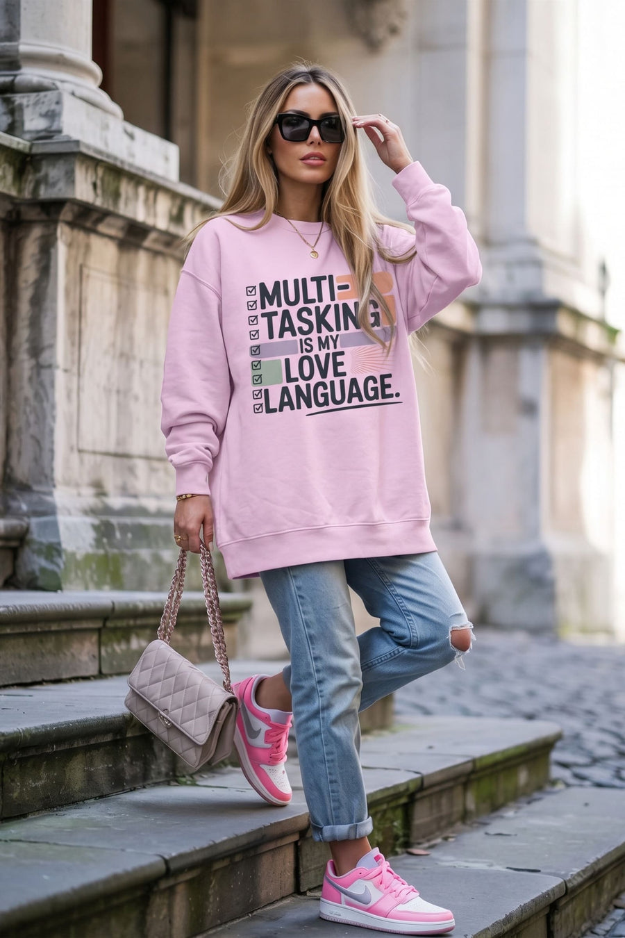 Woman on old stone steps wearing the Love Language™ sweatshirt in Orchid with ripped jeans and a quilted shoulder bag